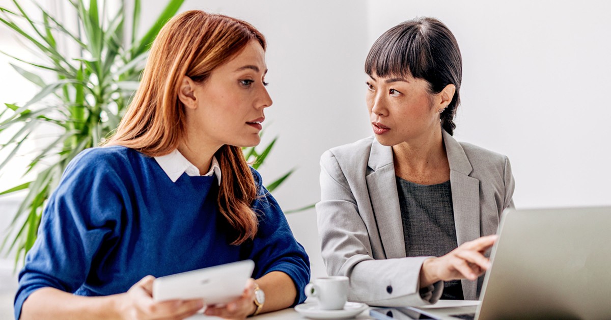 Photo of a woman showing another woman something on a laptop