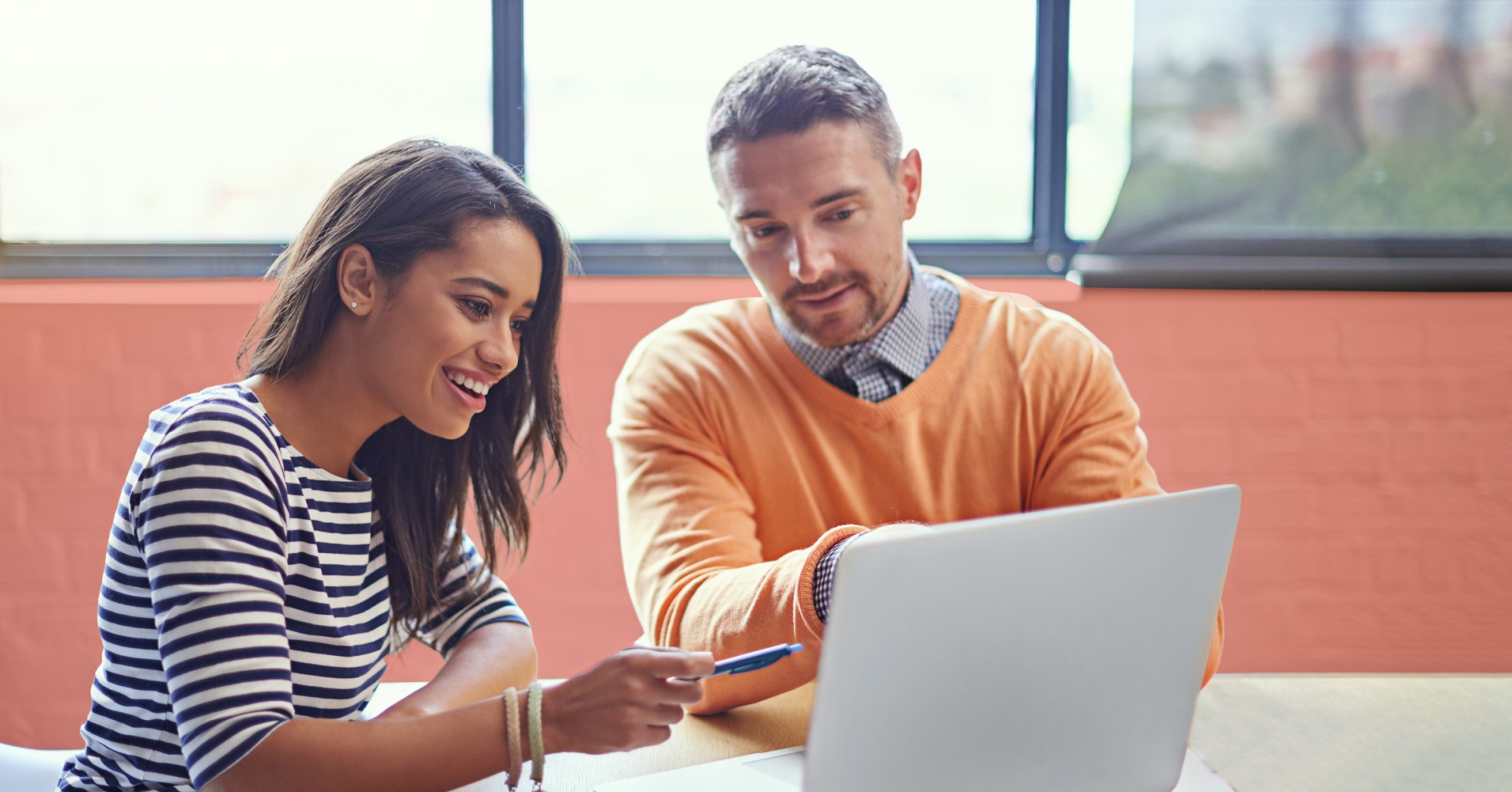 Image of one man and one woman conversing while looking at a laptop