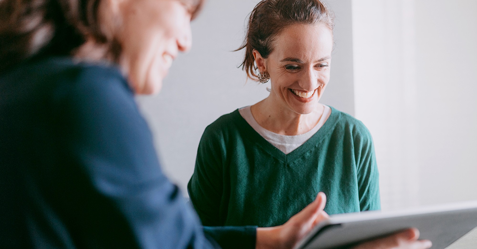 Photo of a woman showing another woman something on a tablet