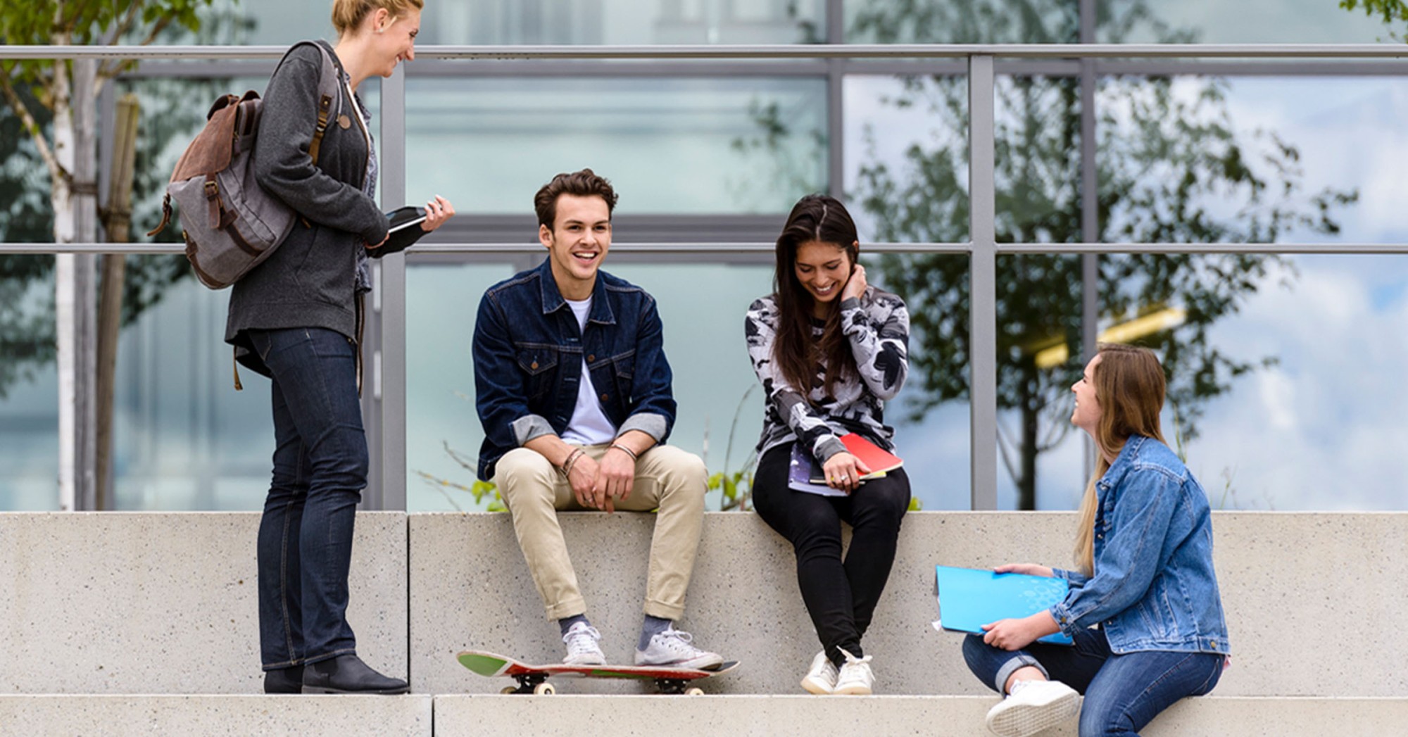 Photo of four students sitting on steps on a college campus talking