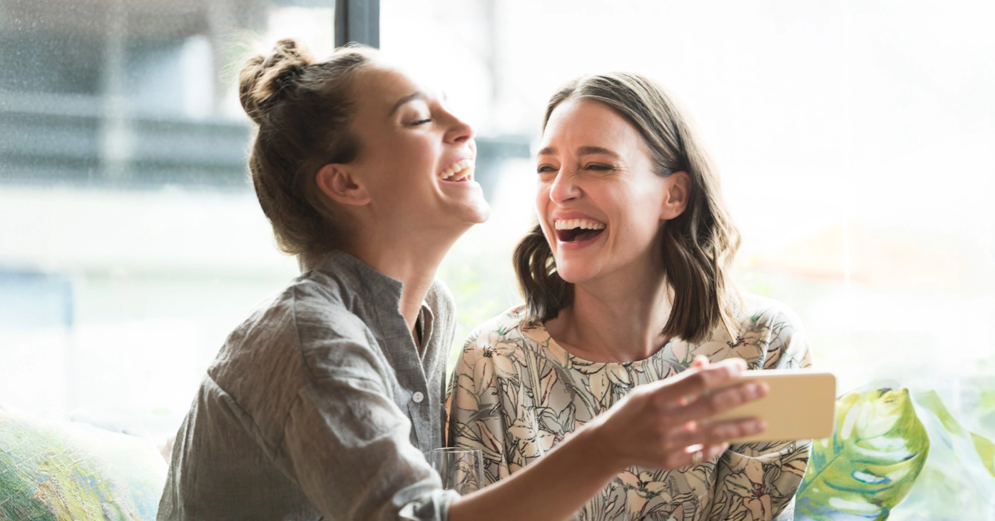 Photo of two women laughing at something on a phone being held