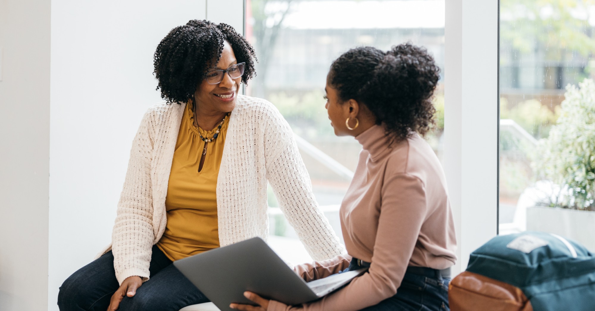 Photo of two women talking while one holds a laptop