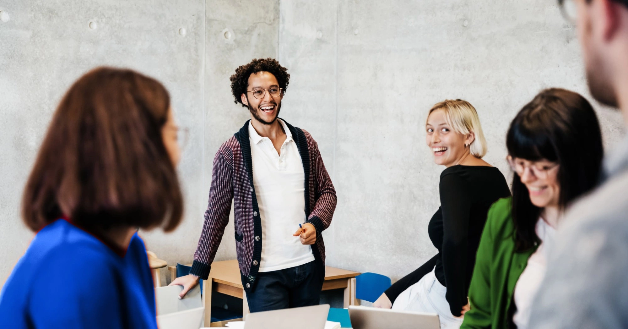 Photo of a diverse group of people talking and laughing around a table in a classroom setting