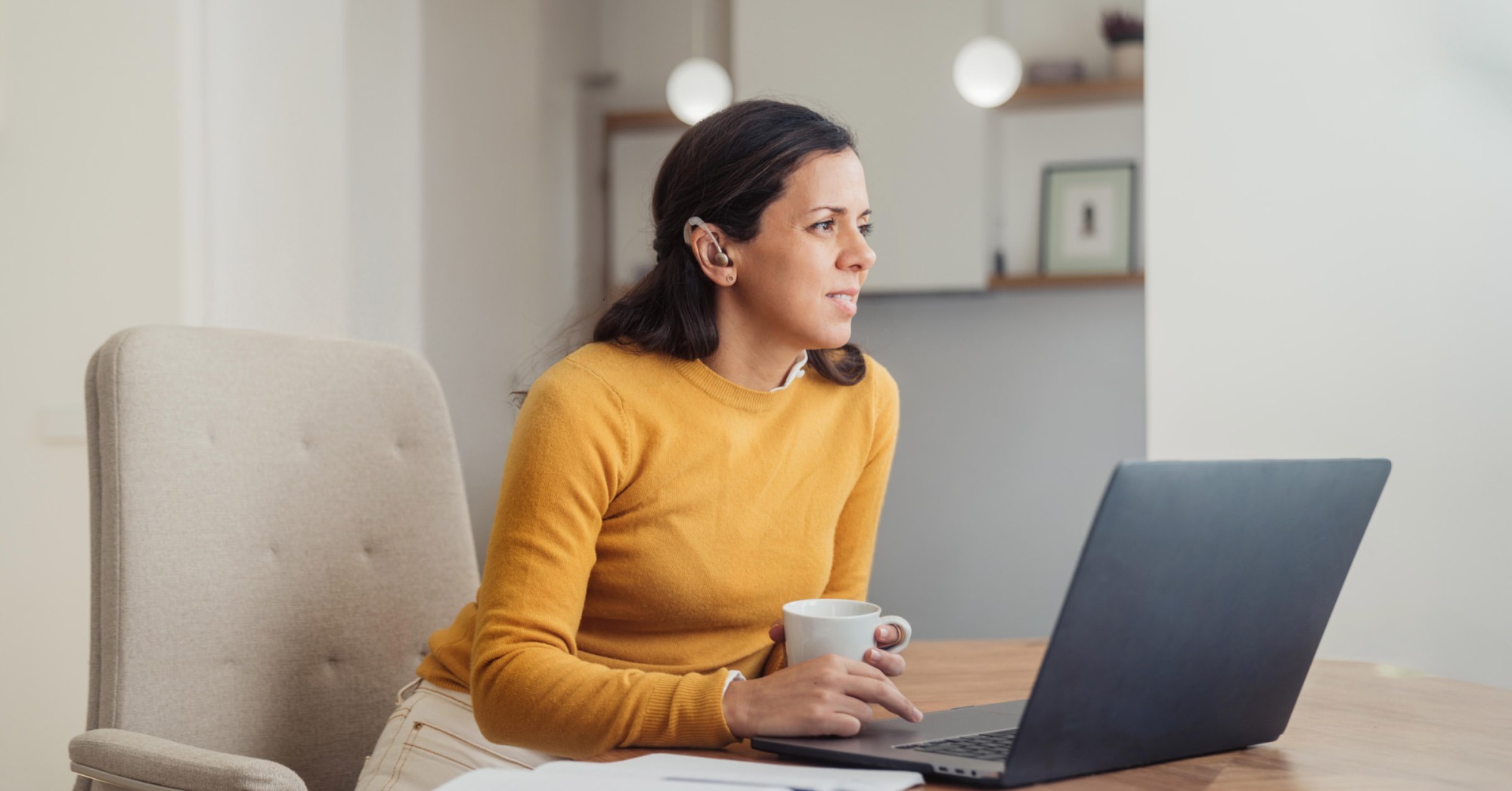 Photo of a woman with a hearing aid working at a laptop